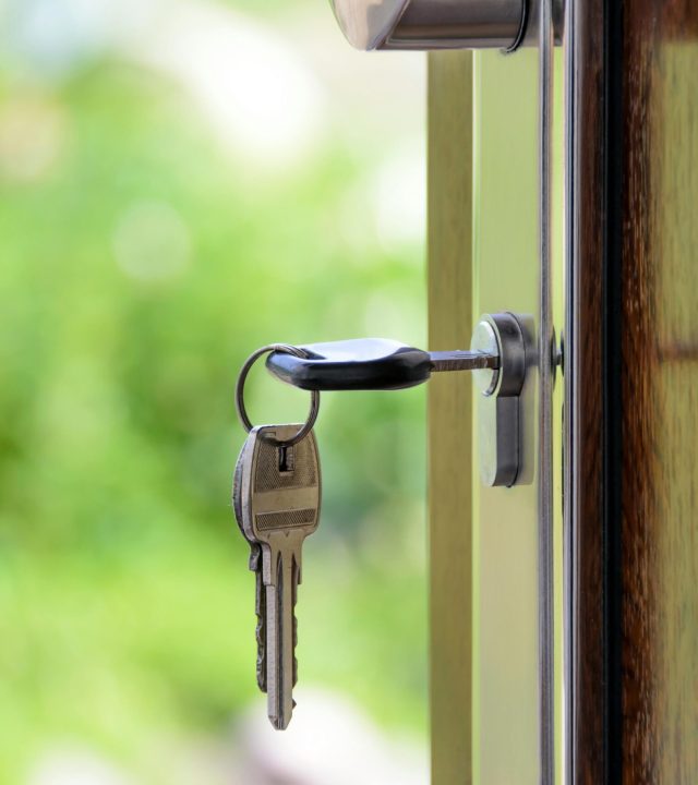 Key inserted in door lock against a blurred green background, symbolizing security and real estate.